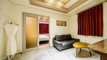 Habitación de hotel con sofá, una mesita redonda, perchero y una puerta corrediza que da a un dormitorio.