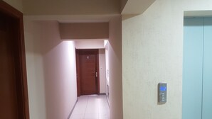 A hallway with a wooden door marked with the number 6, a wall-mounted elevator control panel, and a tiled floor.