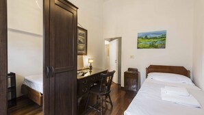 A bedroom with a bed, a desk with a chair, a wardrobe, and a painting on the wall.