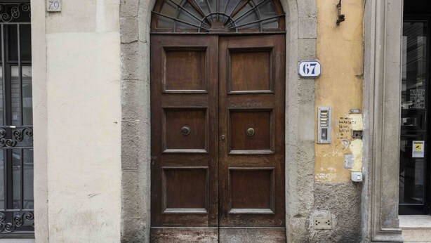 A double wooden door with a fanlight above, a number '67' sign, and a utility box on the wall.