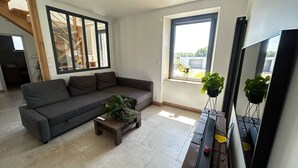 A modern living room with a grey sofa, a wooden coffee table, and a large window with a view of the outdoors.