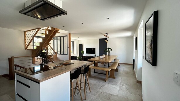 A modern kitchen with a central island, wooden stools, and a dining table.