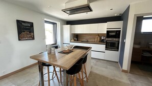 A modern kitchen with white cabinets, a wooden dining table, and a built-in oven.