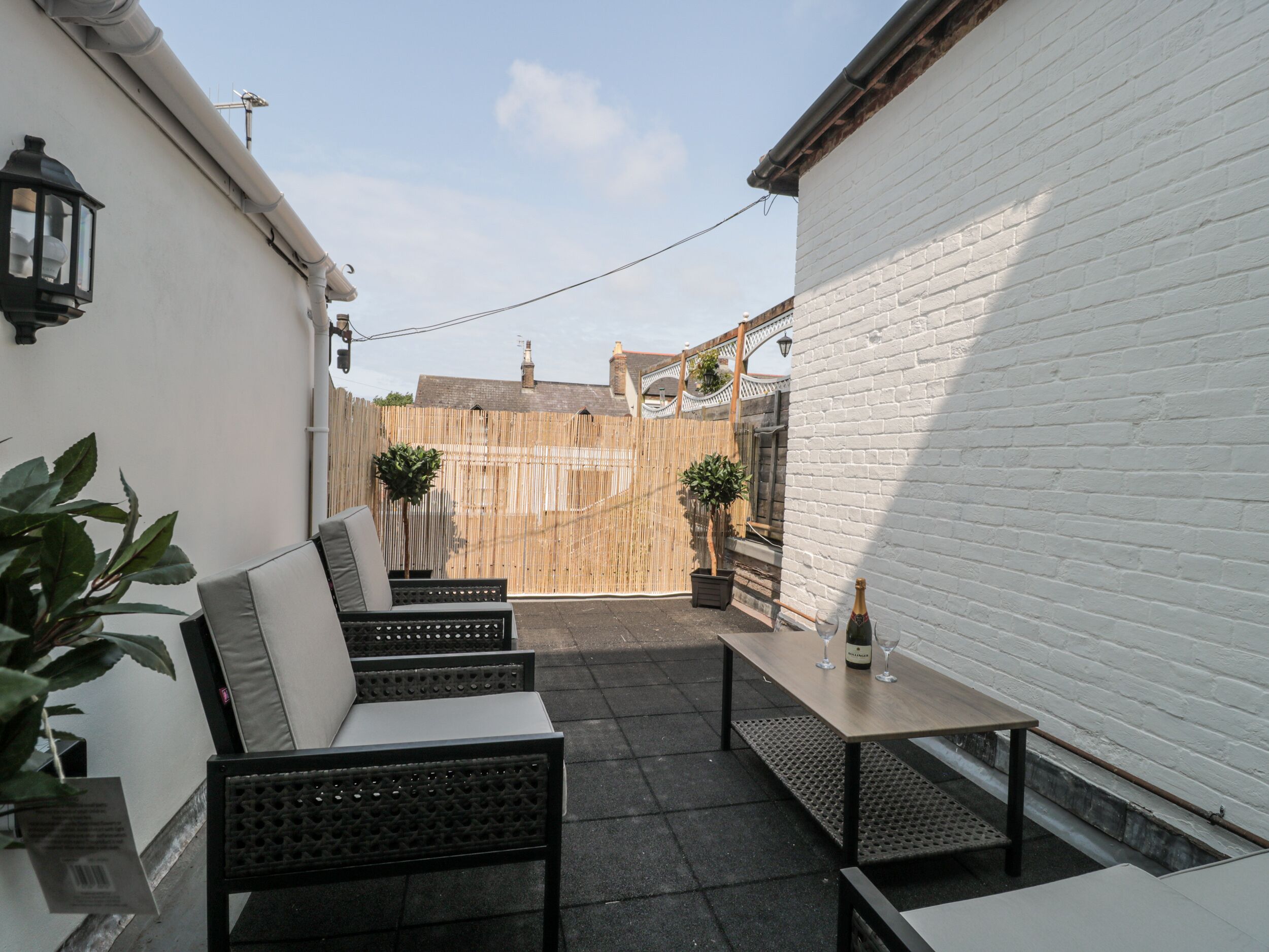 A patio area with outdoor seating, a table with a bottle and glass, and a white brick wall.