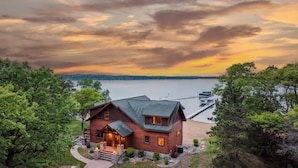 A wooden cabin with a stone pathway leading to the entrance, surrounded by trees and overlooking a lake.