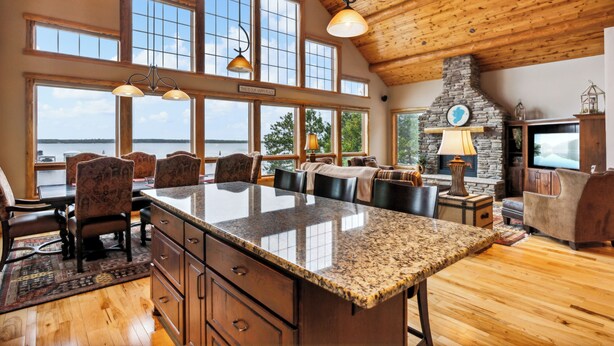 A spacious kitchen with a large island, wooden ceiling, and large windows offering views of the outdoors.