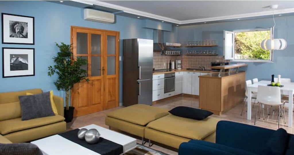 Un espacio habitable compacto con kitchenette, comedor y zona de estar con sofá y mesa.