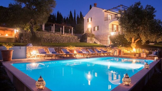 A poolside area with lounge chairs, a stone wall, and a building in the background.