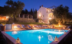 Un área junto a la piscina con sillones de descanso, un muro de piedra y un edificio al fondo.