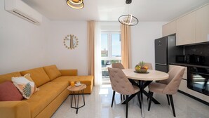 A modern kitchen with a dining area, a sofa, and a small table with a fruit bowl.