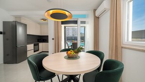 A modern kitchen with a built-in refrigerator and stove, a dining area with a round table and four chairs, and a large window with a view of a pool and buildings.