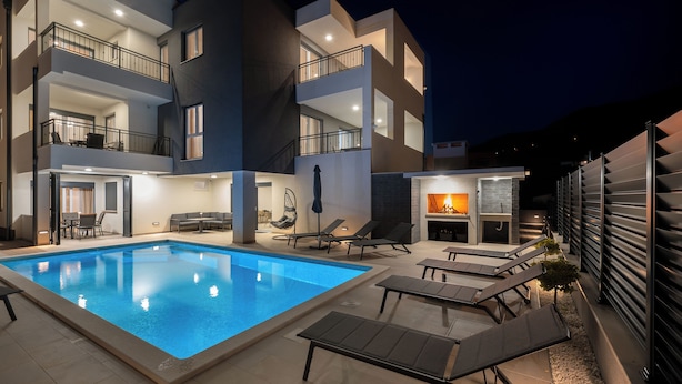 A modern building with a swimming pool, outdoor seating, and a fireplace.