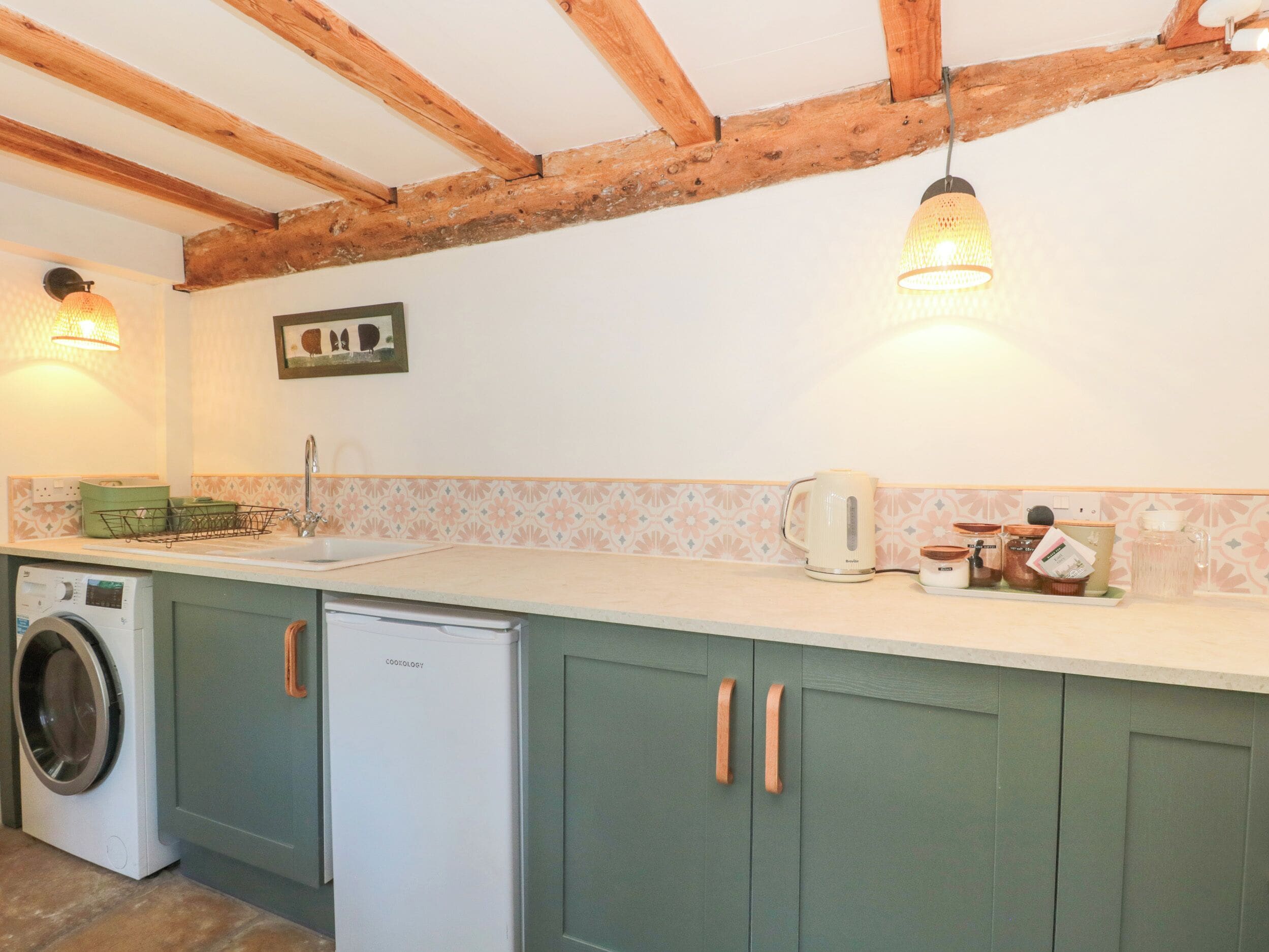 A kitchen with wooden beams, a washing machine, a refrigerator, and a coffee maker.