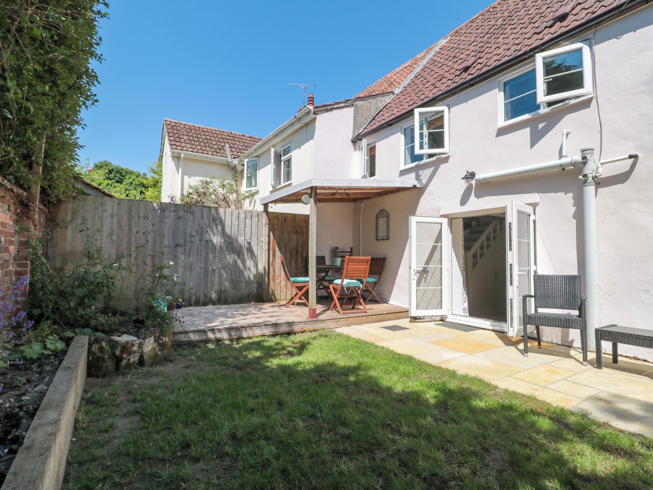 A two-story house with a patio area, a wooden fence, and a grassy yard.