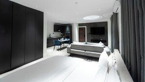 A modern hotel room with a large bed, a sofa, a dining table with chairs, a kitchen area, and a TV mounted on the wall. - The VVS Apartments - Studio Apartment with Balcony (Accra)