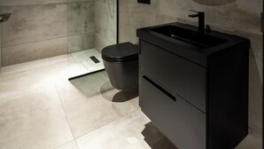 A modern bathroom with a glass shower enclosure, a round mirror, and a black vanity. - The VVS Apartments - Studio Apartment with Balcony (Accra)