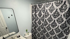 Un baño con lavamanos blanco, espejo, inodoro y cortina de ducha negra.