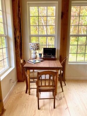 A room with a wooden table, two chairs, a lamp, and a window with a view of trees.