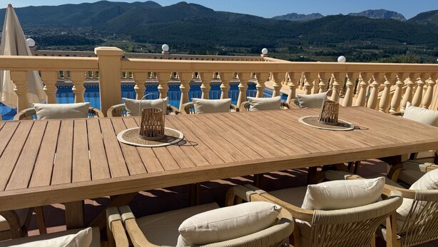 A wooden deck with wicker chairs and a table, overlooking a pool and mountains. - Villa Almazara (Xalo)