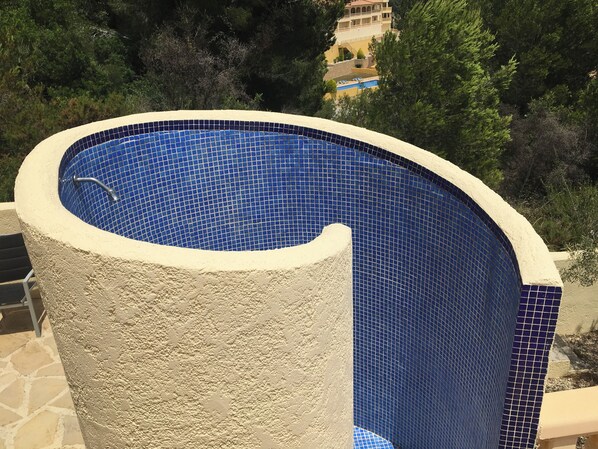 A round swimming pool with blue mosaic tiles and a textured beige wall.