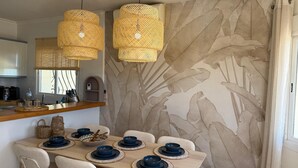 A dining area with a wooden table set for six, surrounded by wicker pendant lights and a leaf-patterned wall. - Villa Almazara (Xalo)