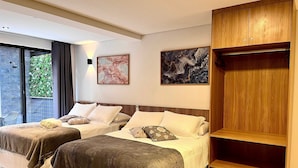 A modern bedroom with two beds, a wooden wardrobe, and a large window offering a view of greenery. - Hyde Park Select - by Living (Joao Pessoa)