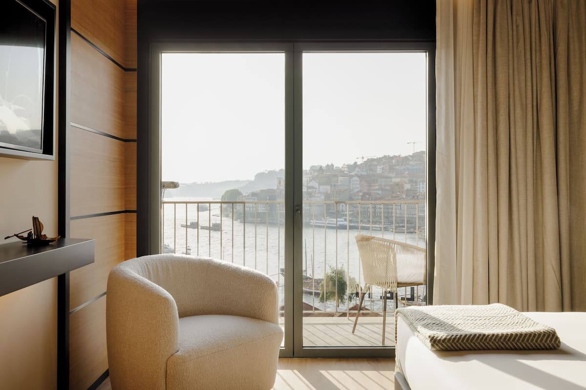 A modern hotel room with a large sliding glass door leading to a balcony with a city view.
