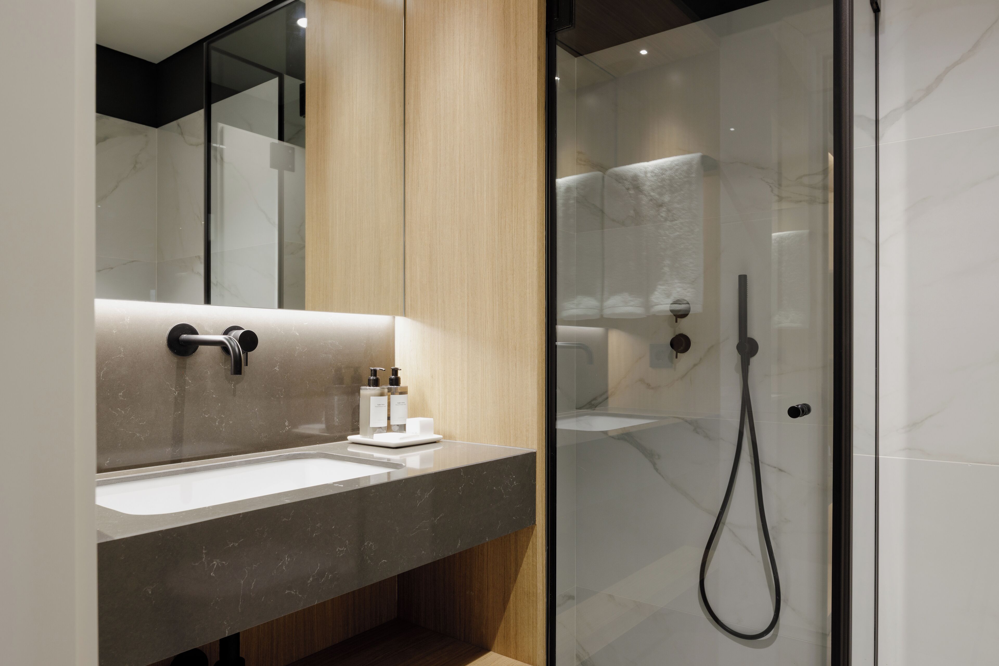 Un baño moderno con lavamanos de mármol, paneles de madera y cabina de ducha con paredes de vidrio.