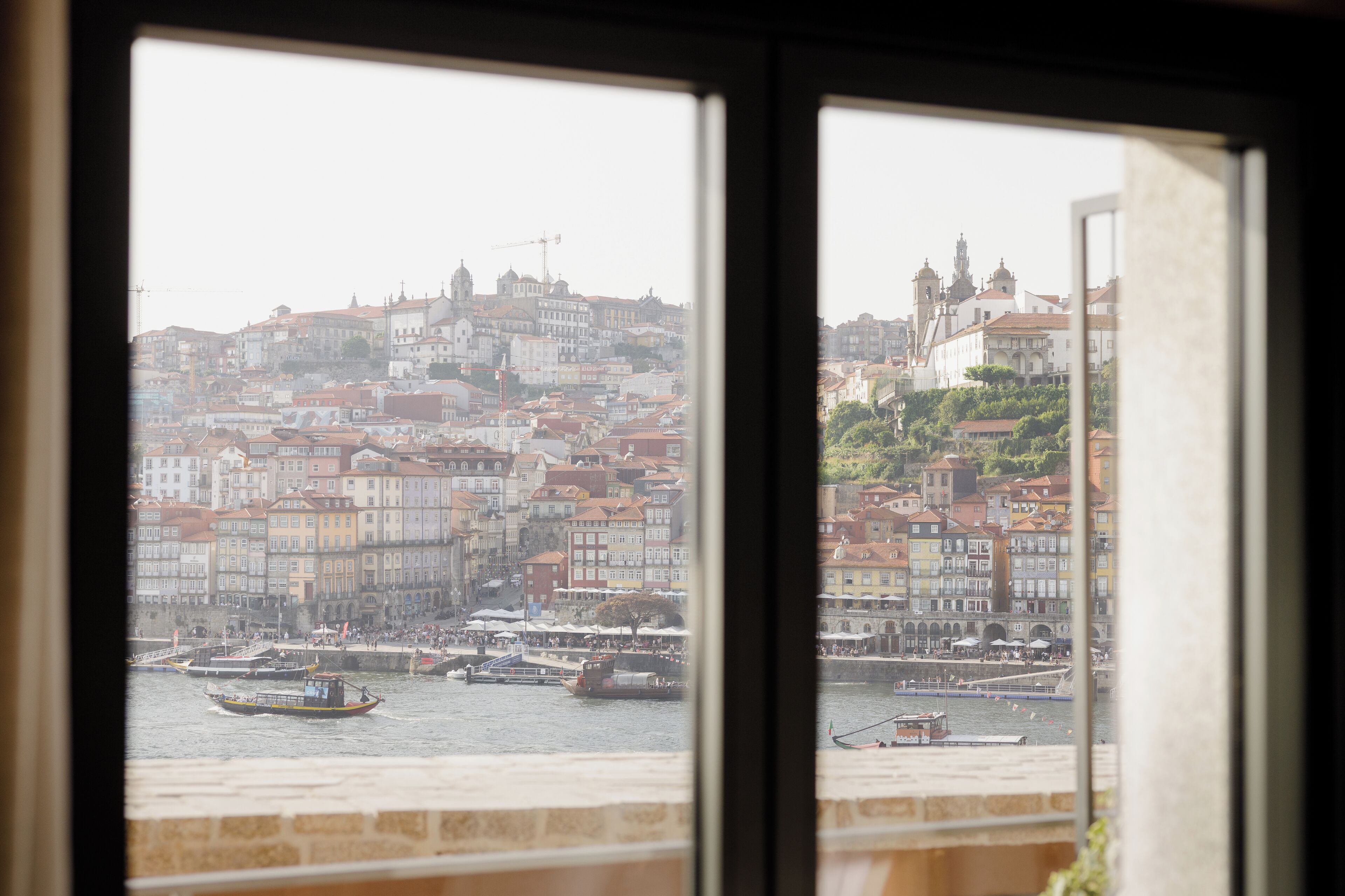 A view of a cityscape through a window, featuring a river with boats and buildings along the riverbank.