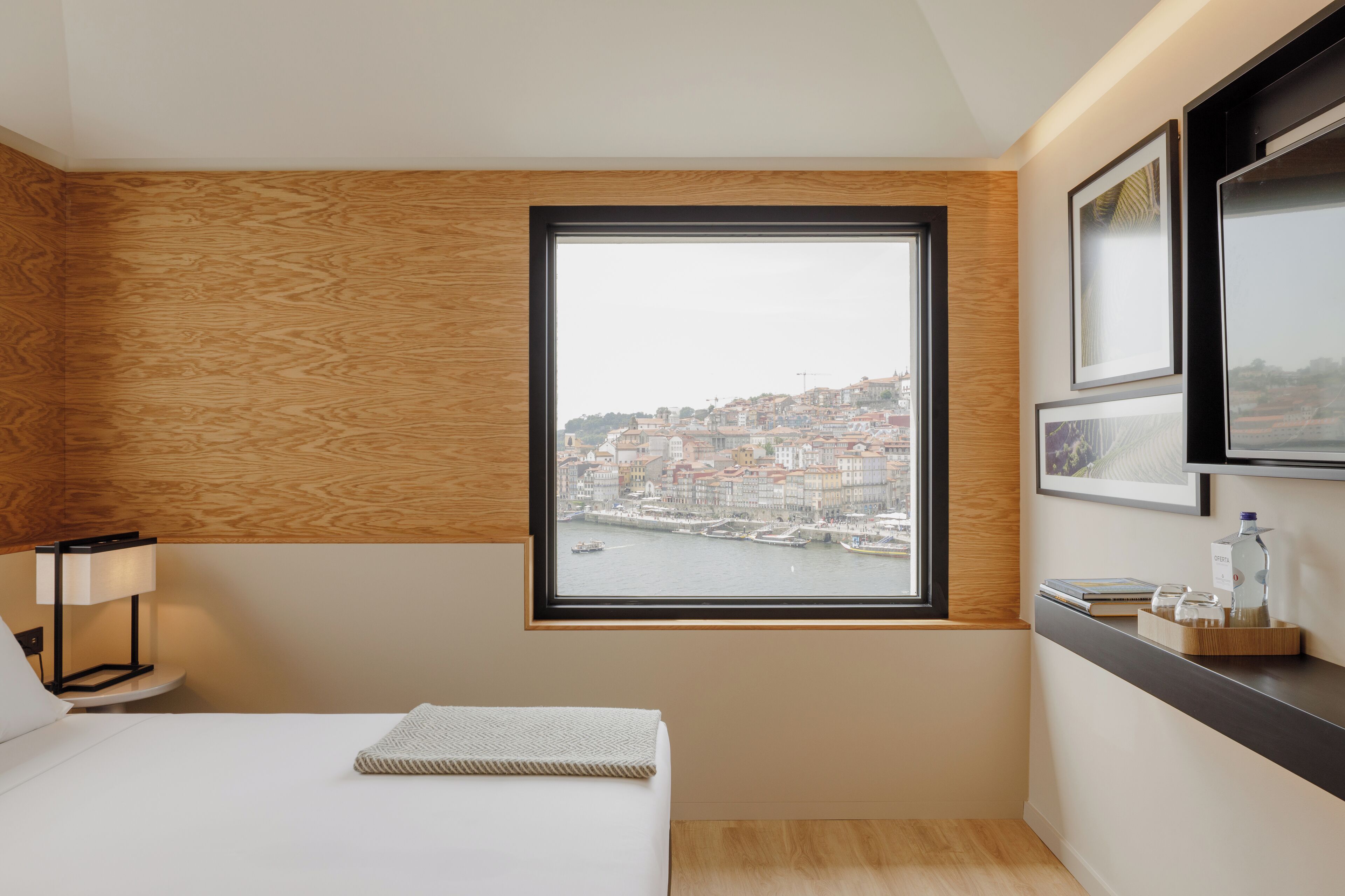 Habitación de hotel con un amplio ventanal que ofrece vistas a un paisaje urbano y al río.