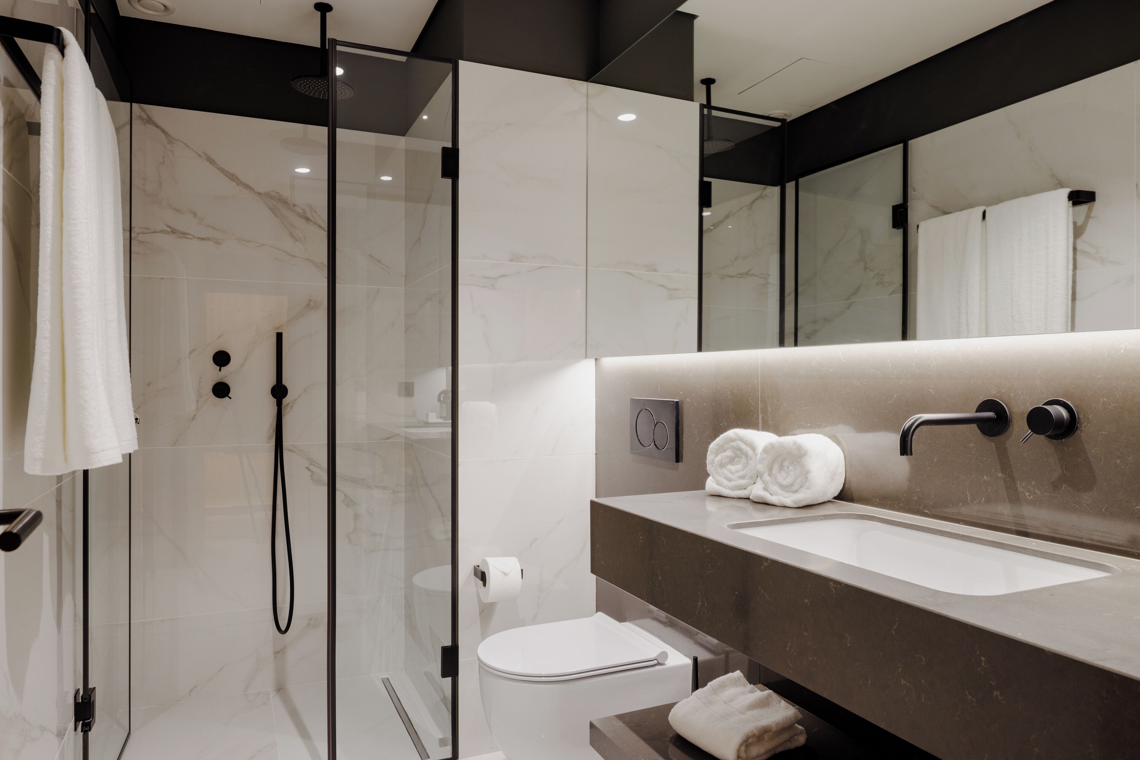 A modern bathroom with a glass-enclosed shower, a toilet, and a sink with a towel rack.
