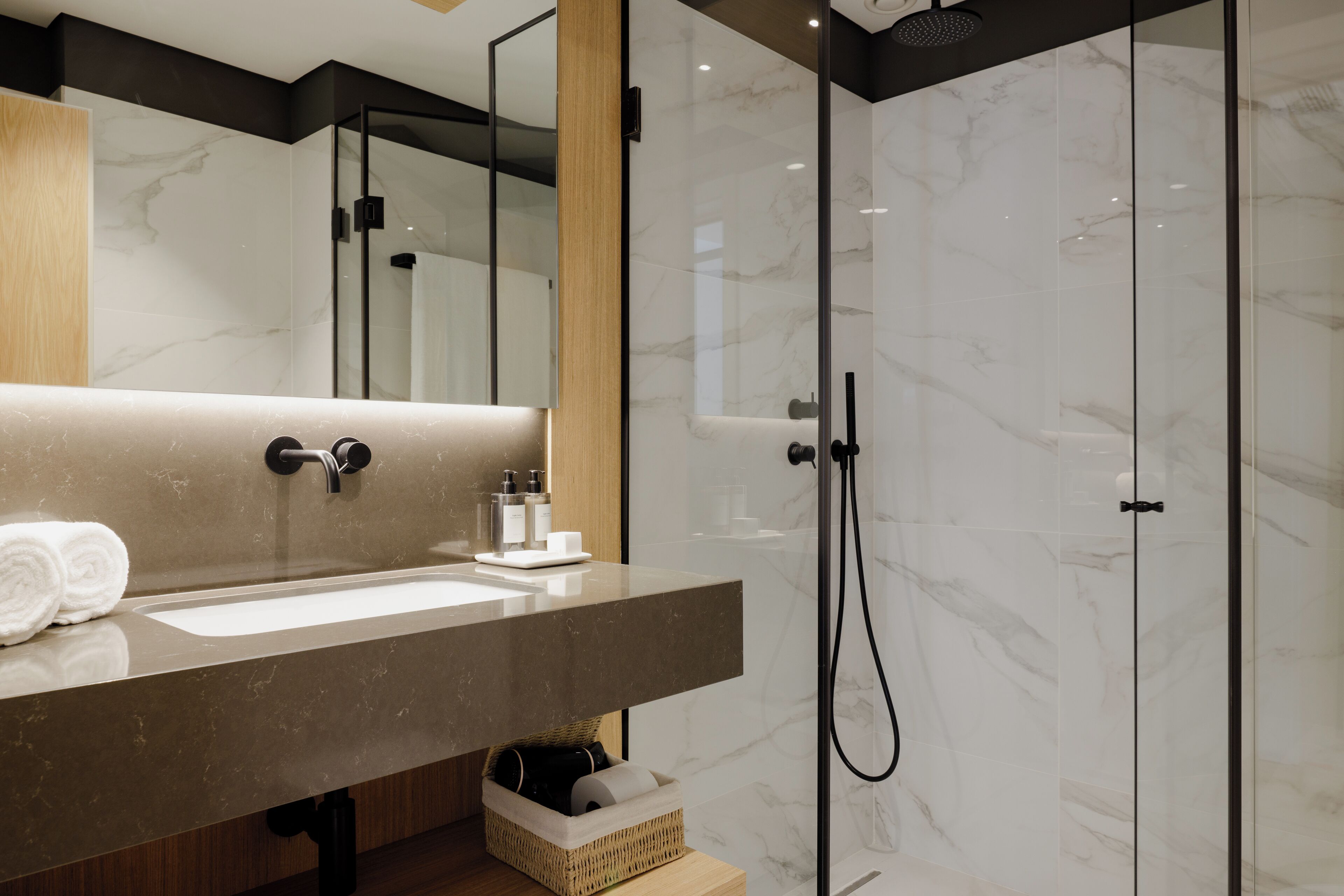 Een moderne badkamer met een marmeren wastafel, een douche met glazen wanden en een houten opbergmeubel.