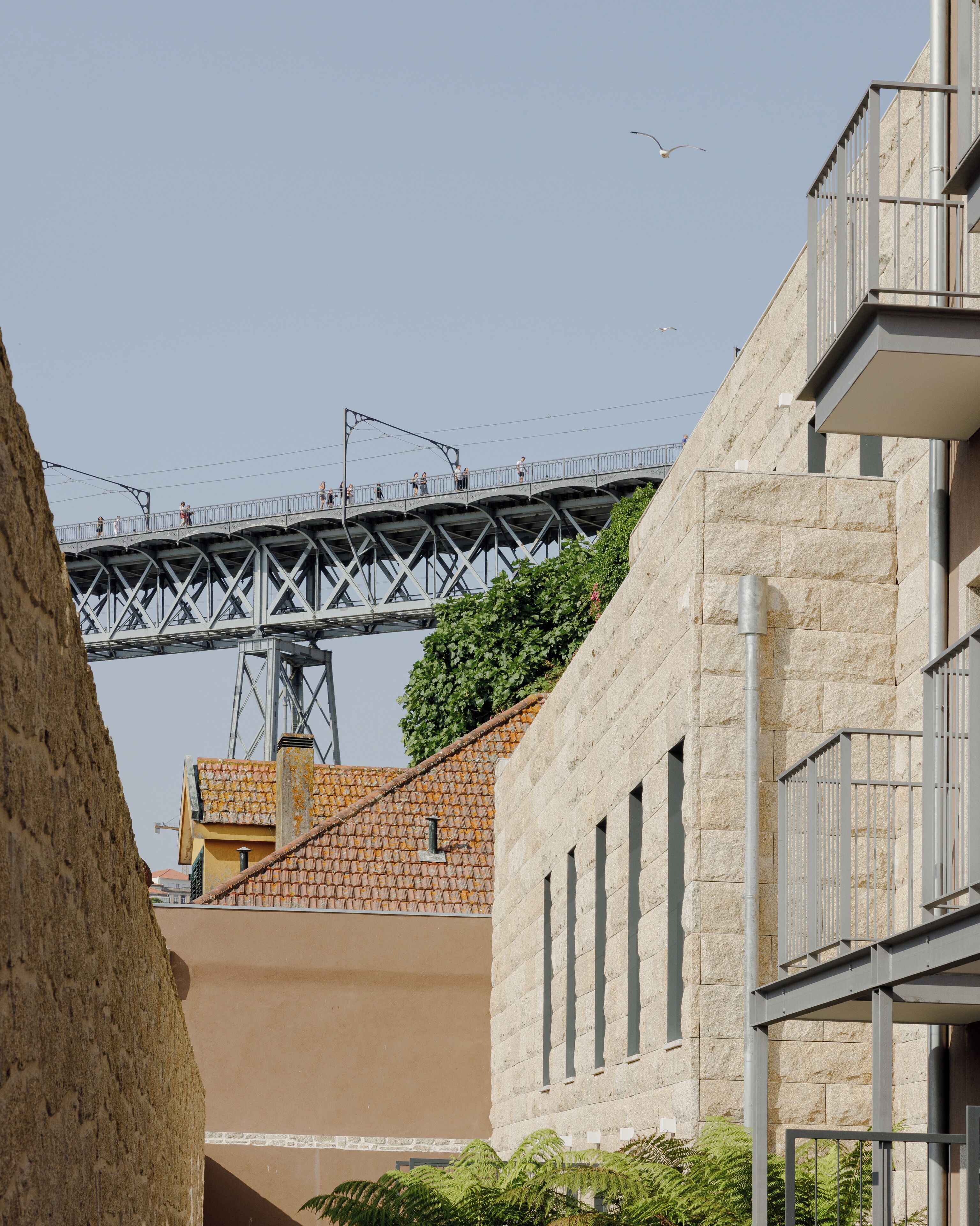 A bridge with people walking on it, a building with a stone facade, and a tree in the foreground.