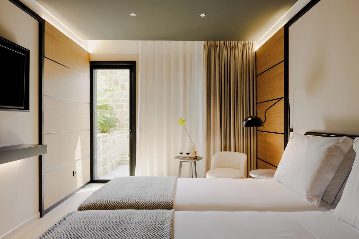 A modern hotel room with a large bed, a small side table, a chair, and a TV mounted on the wall.