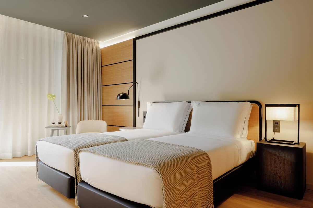 A double bed with a wooden headboard, two bedside tables, a lamp, and a small table with a vase and candle.