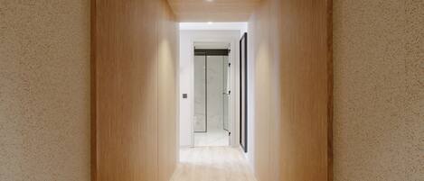 A narrow hallway with wooden walls and a light wooden floor, leading to a glass door.