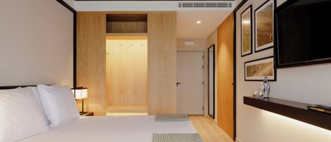 Une chambre d’hôtel moderne avec un grand lit, une armoire en bois, un téléviseur fixé au mur et des œuvres d’art encadrées.