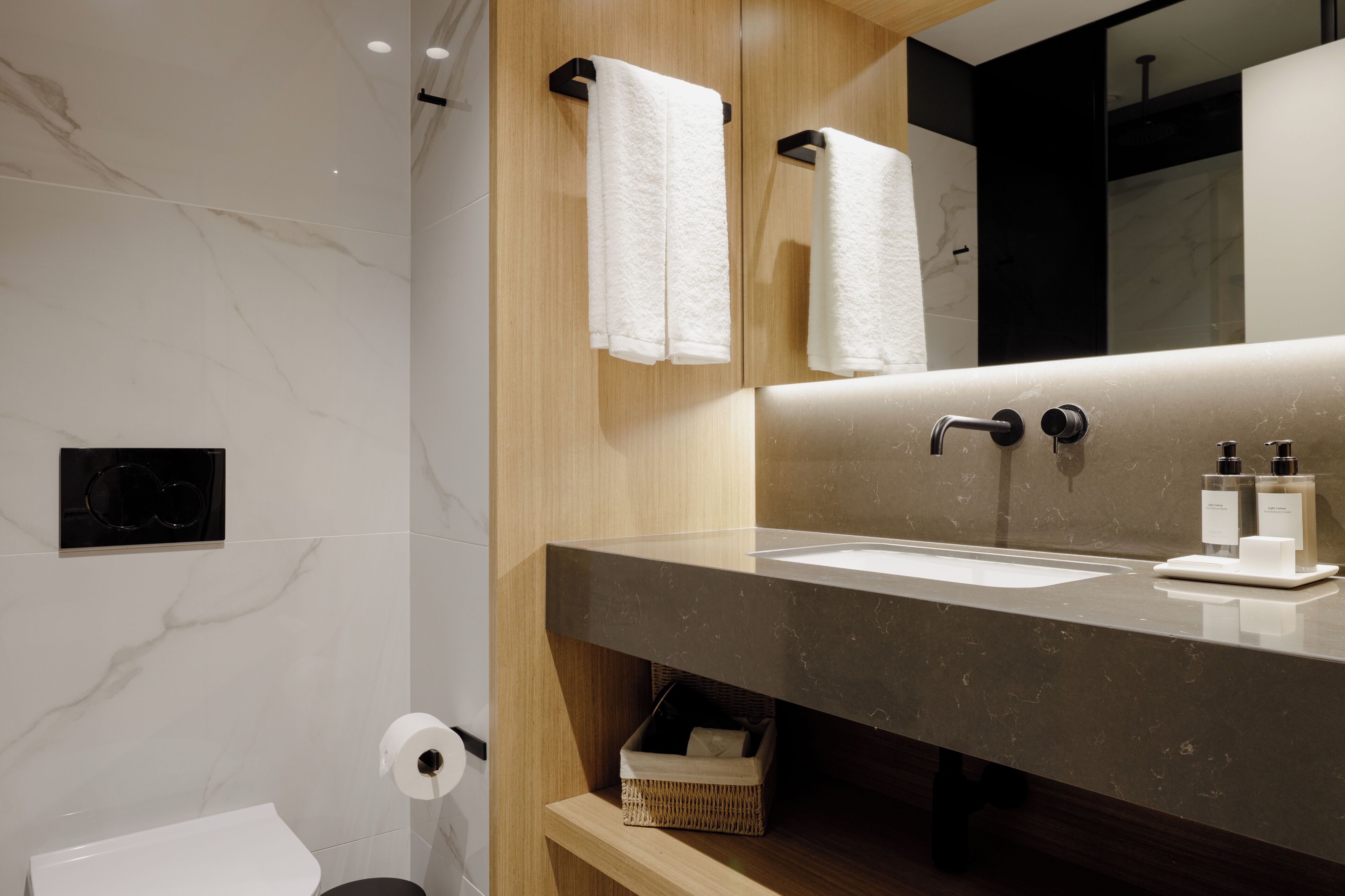 Un baño moderno con pared de mármol, tocador de madera, espejo grande y dos toallas blancas colgadas en ganchos.