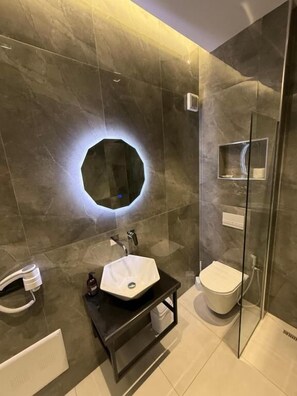 A modern bathroom with a hexagonal mirror, a white sink, and a toilet. - Day LUX Premium Apartments (Sarandë)