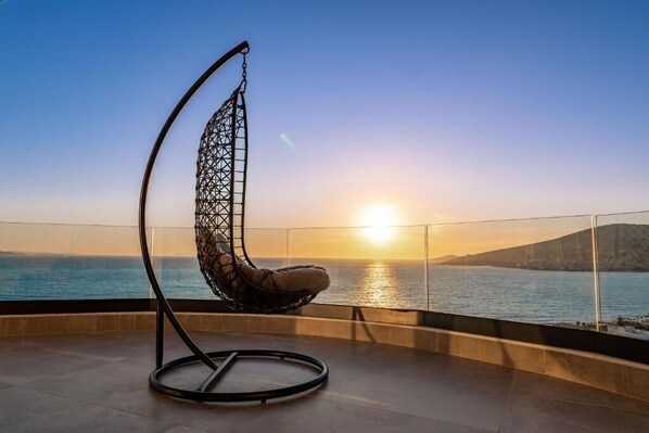 A hanging chair on a balcony with a sunset view.