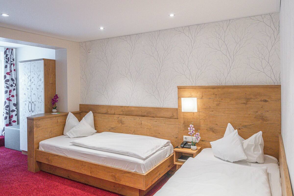 Ein Hotelzimmer mit zwei hölzernen Betten, einem roten Teppich und einem Nachttisch mit Lampe und Telefon.