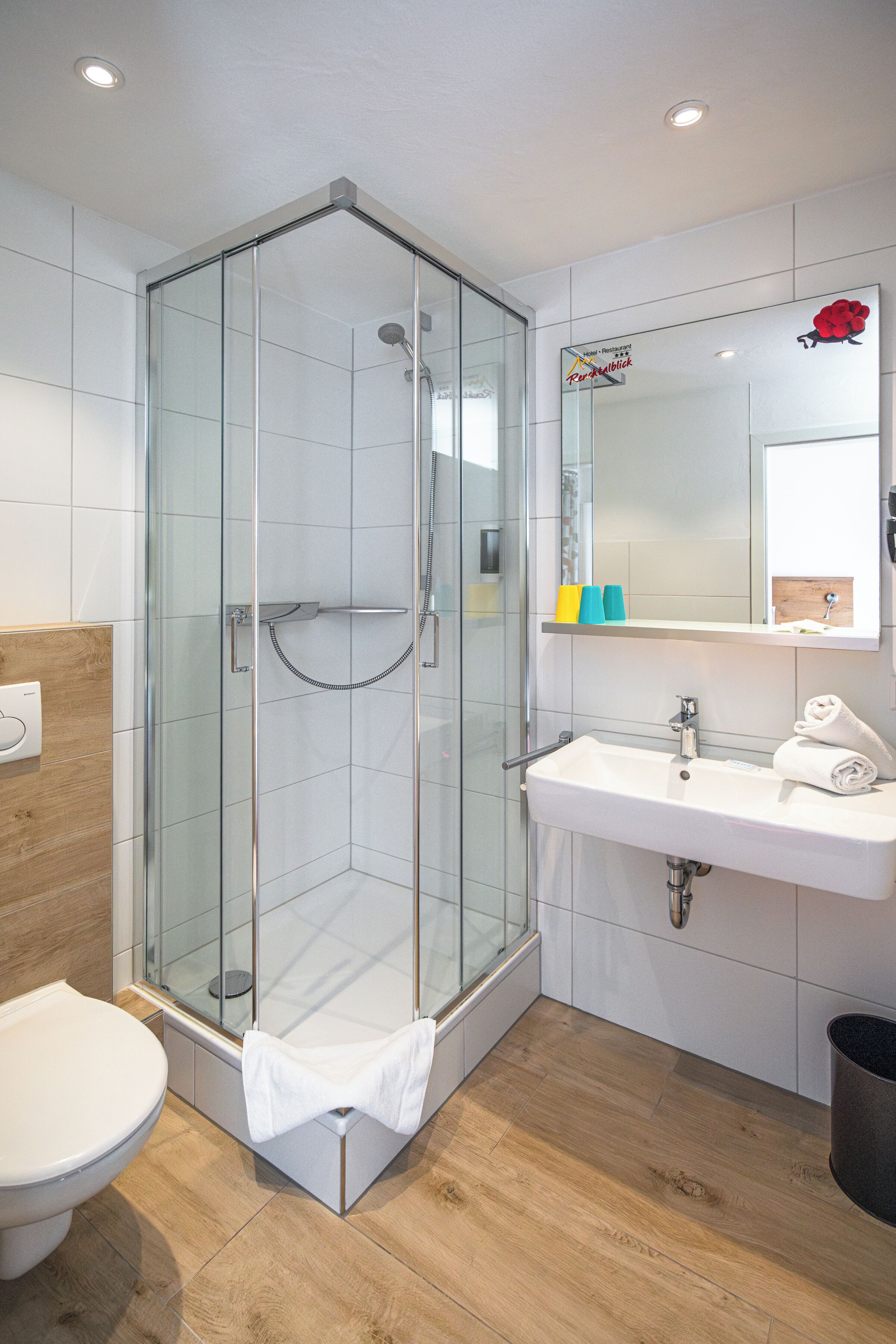 Une salle de bain moderne avec une douche en verre, un lavabo blanc et un miroir orné d’une rose rouge.