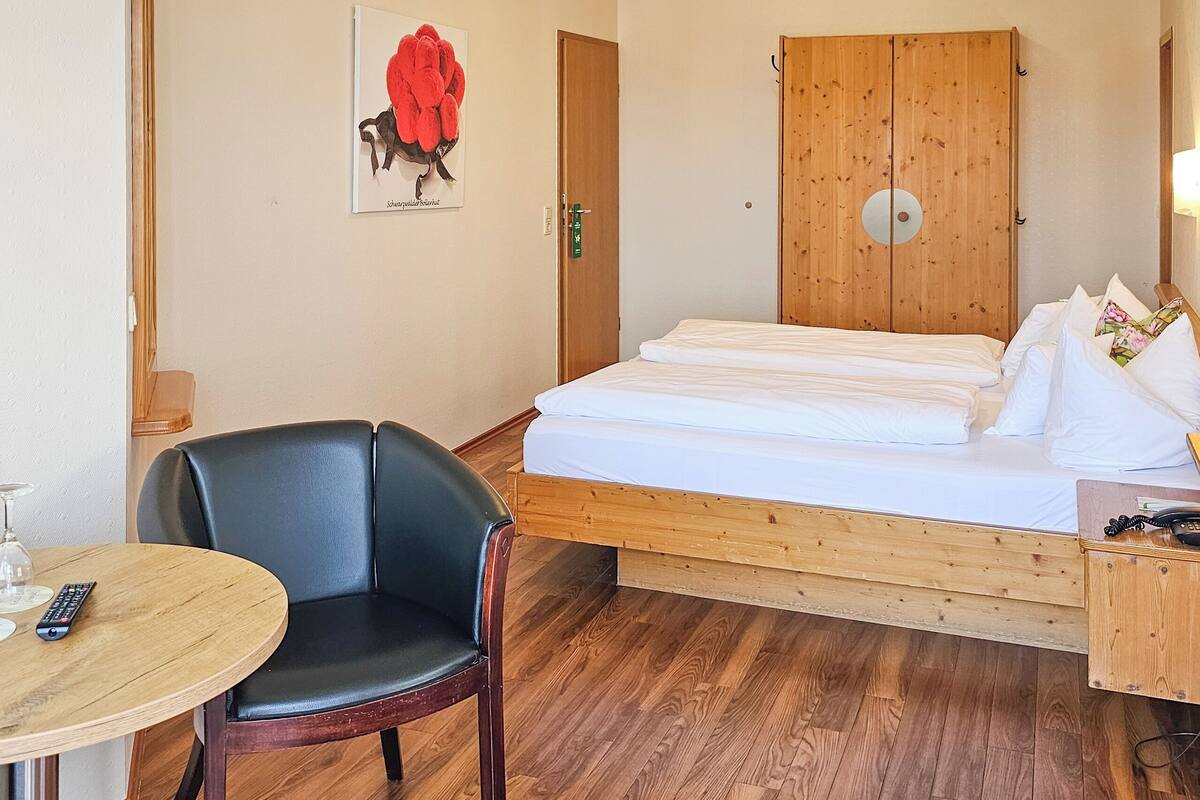 Ein Hotelzimmer mit einem Bett, einem Sessel, einem Tisch mit Fernbedienung und einem Telefon.