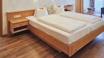 Ein hölzernes Bett mit weißer Bettwäsche, ein Nachttisch und eine kleine Holzablage.