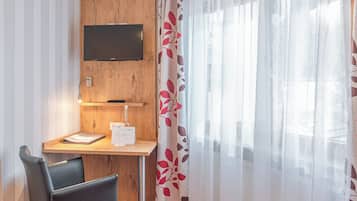 Une chambre d’hôtel avec un bureau en bois, une chaise noire, un téléviseur fixé au mur et une moquette rouge.