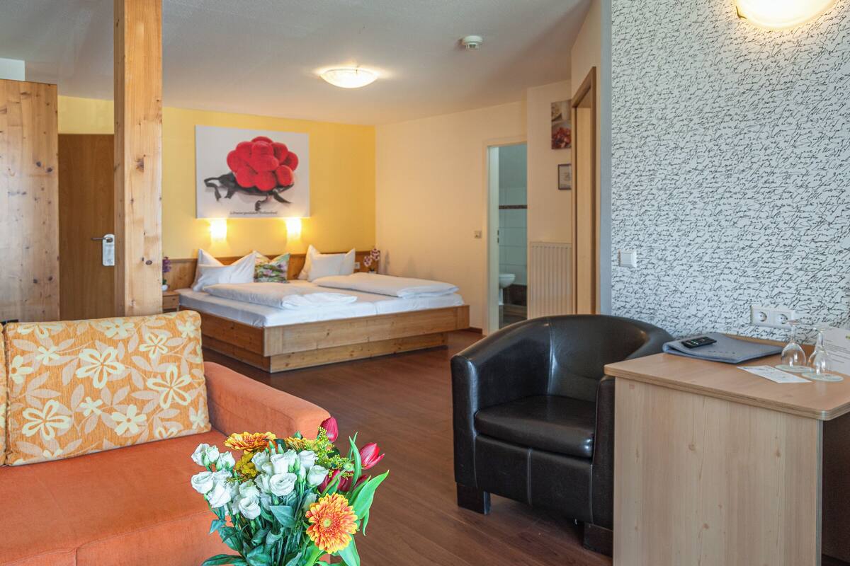 Ein Hotelzimmer mit Bett, einer Sitzecke inklusive Sofa und Tisch sowie einem kleinen Schreibtisch mit Stuhl.