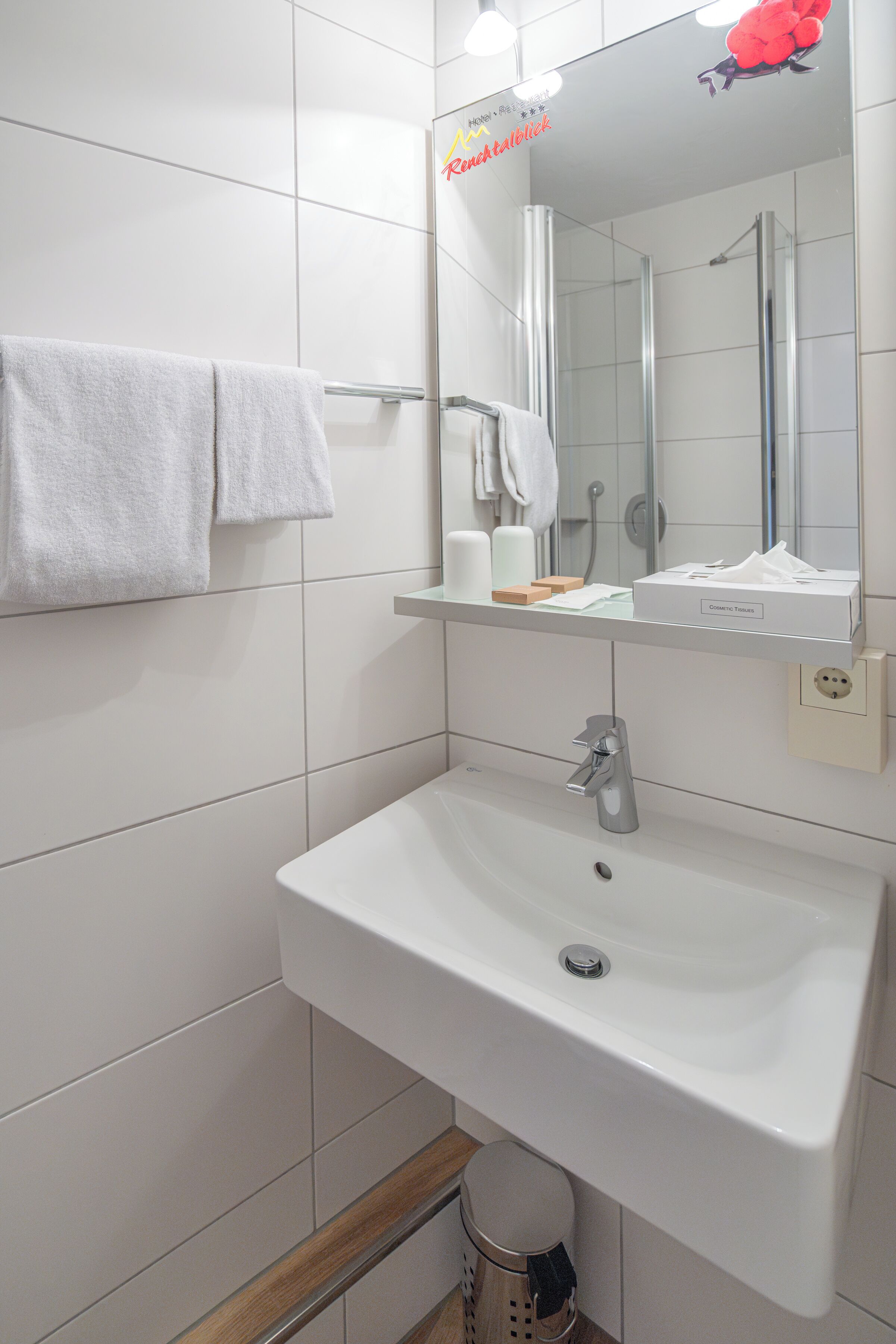 Un baño con lavamanos blanco, un espejo y un perchero para toallas.