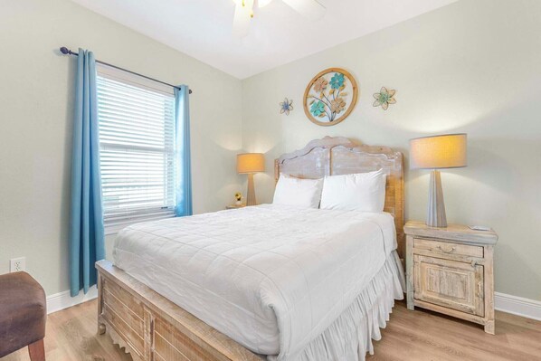 A bedroom with a bed, two bedside tables, a nightstand, a window with curtains, and a wall with floral decorations.