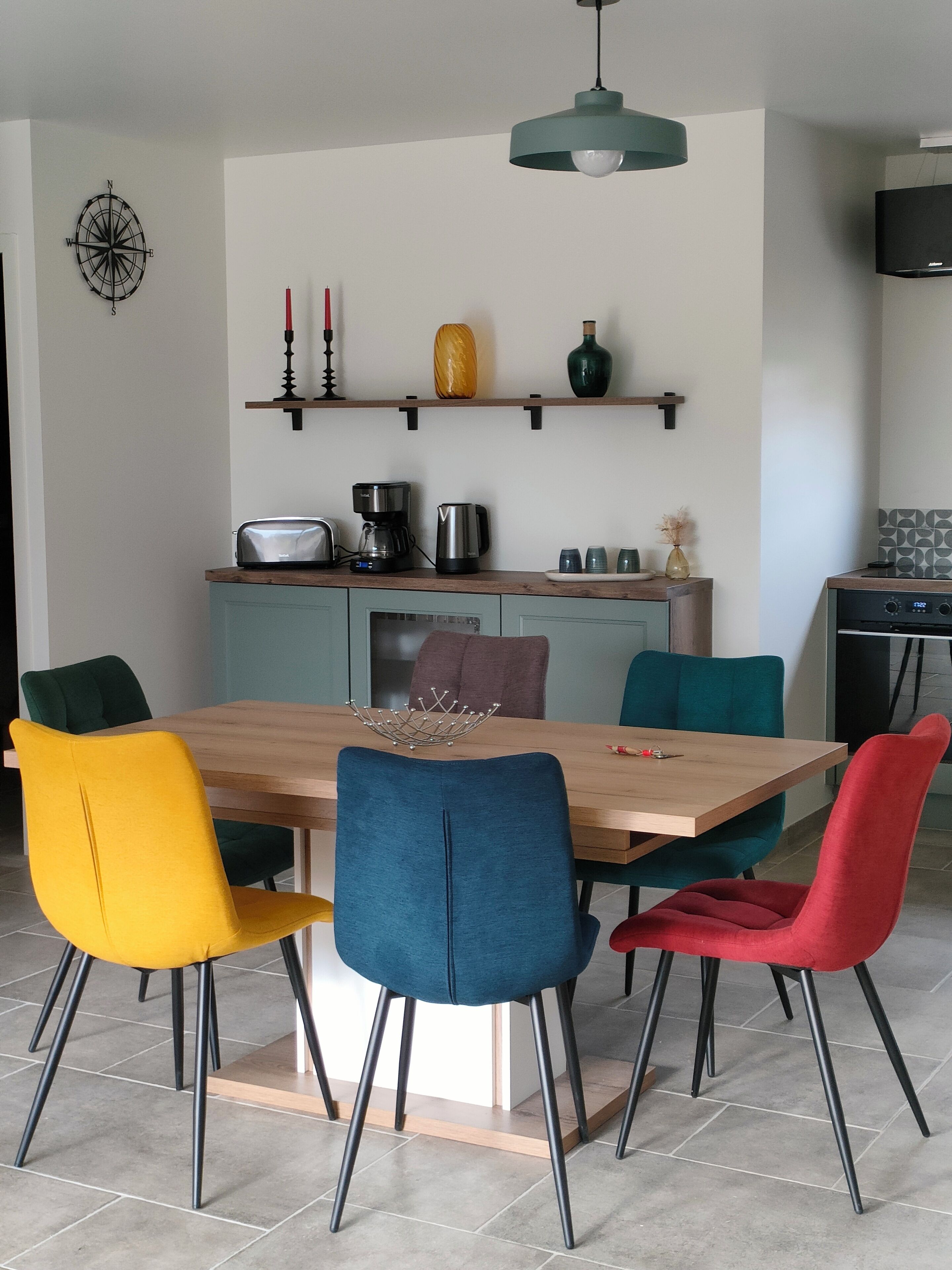 Eine moderne Küche mit einem Holztisch, bunten Stühlen und einem Wand-Fernseher.