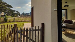 A view from a room with a sliding glass door to a backyard with a wooden fence, a lawn, and a distant view of houses and trees.
